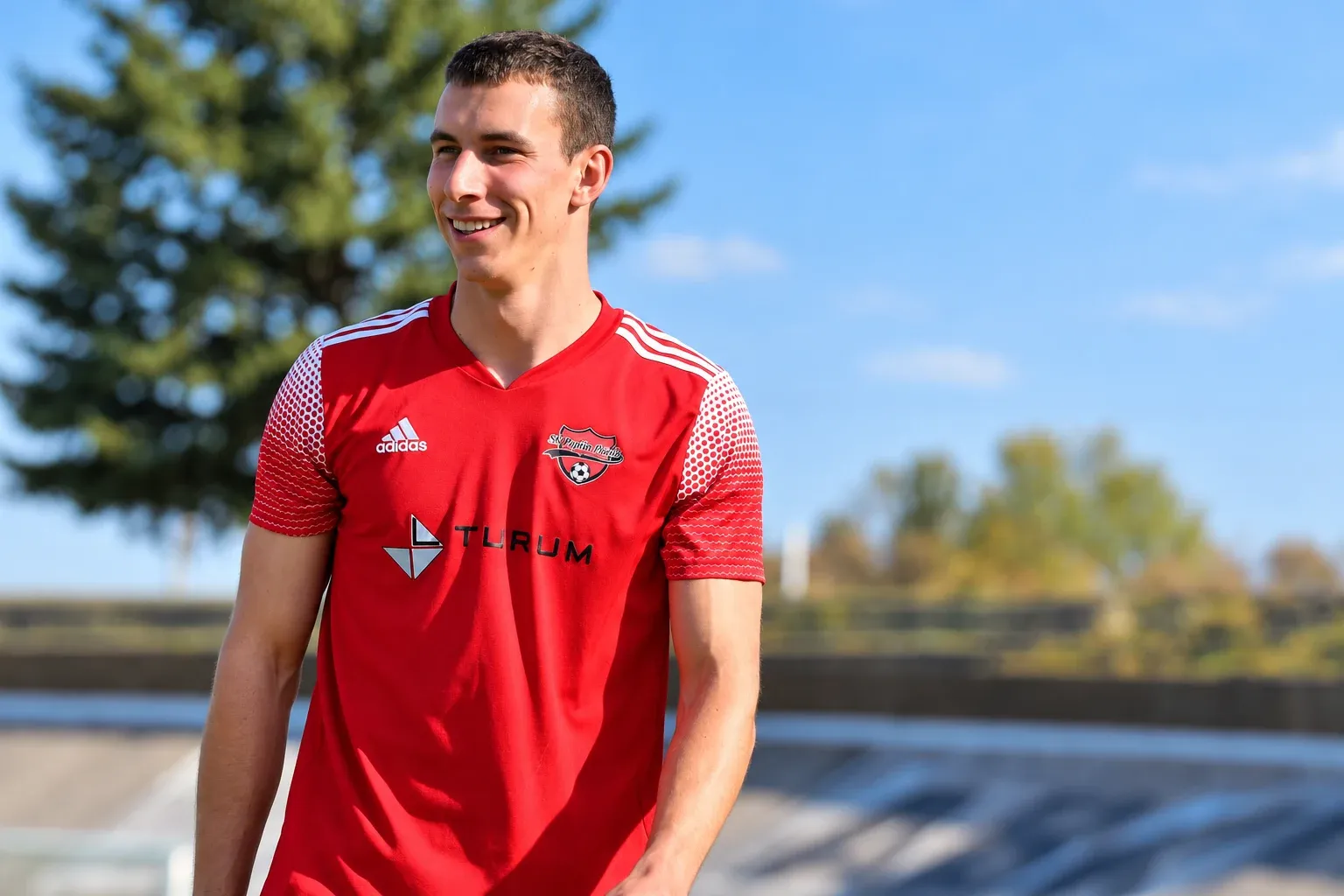 Michal Provod smiling in a red football shirt at a sports ground.