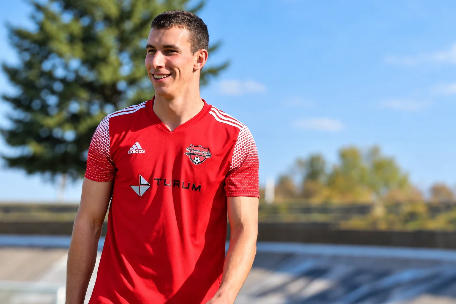 Michal Provod smiling in a red football shirt at a sports ground.