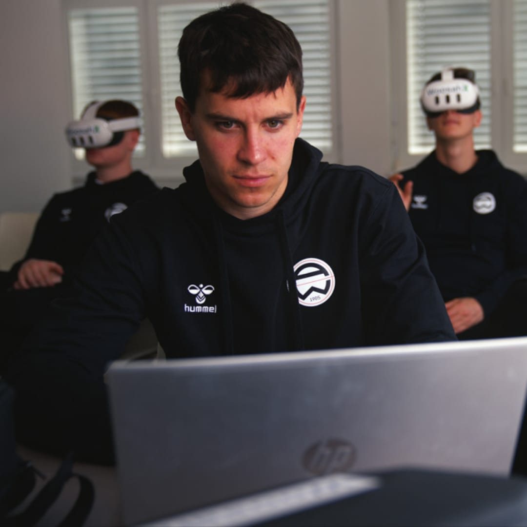 Club staff member using a laptop while athletes train with WoosahX VR headsets